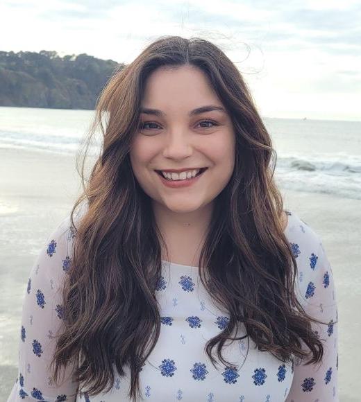 Headshot of Jessica Mangili smiling and standing in front of a beach landscape. 