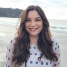 Headshot of Jessica Mangili smiling and standing in front of a beach landscape. 